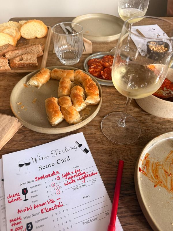 Ingevulde score card naast een glas witte wijn en een bord met hapjes